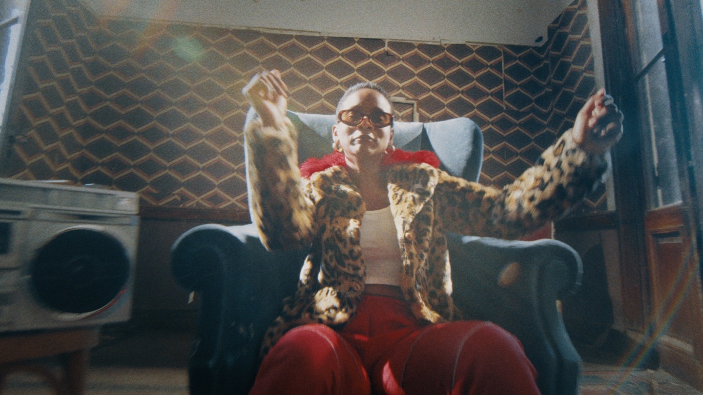 Performer seated on a sofa in a patterned retro room